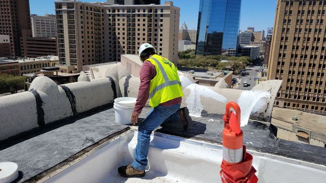 A Longhorn roofer working on a rooftop with the Fort Worth skyline behind him