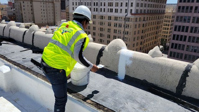 A Longhorn roofing technician sealing a rooftop seam on a downtown commercial building